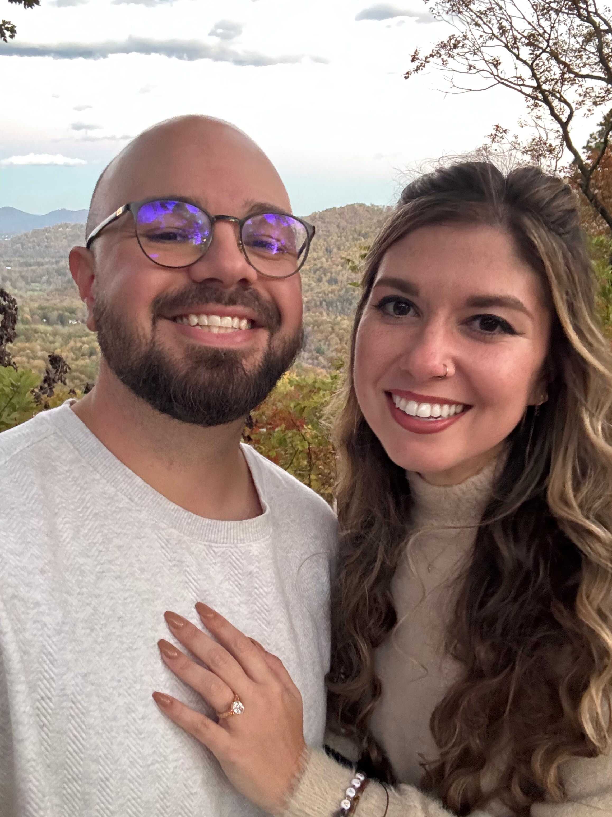 A close portrait of the two of them cheek to cheek, one hand resting on the other’s chest with an engagement ring on it.