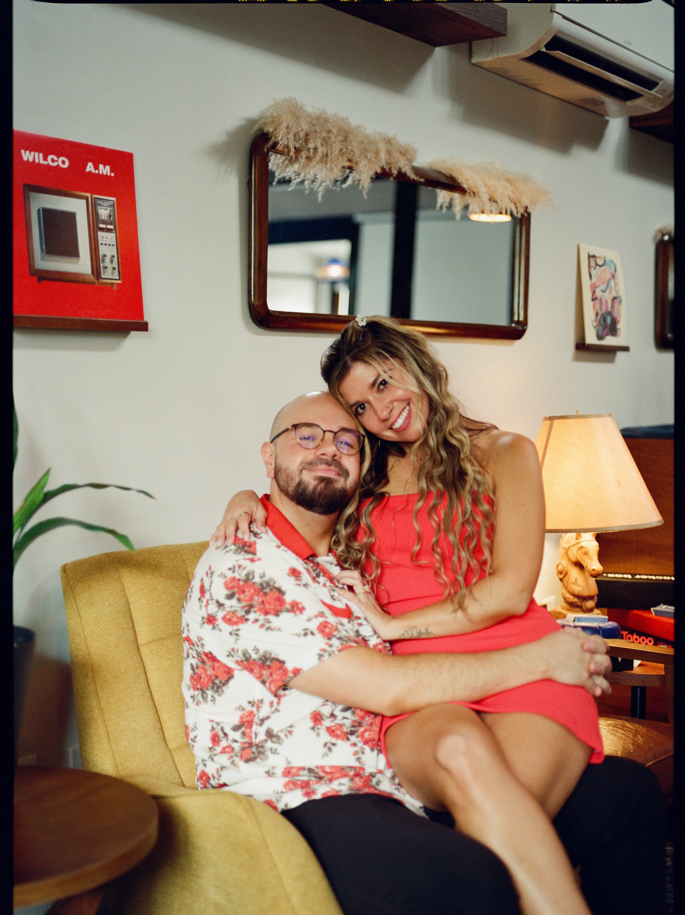 Curled up together in a mustard armchair in a room of vintage furniture and lamplight.