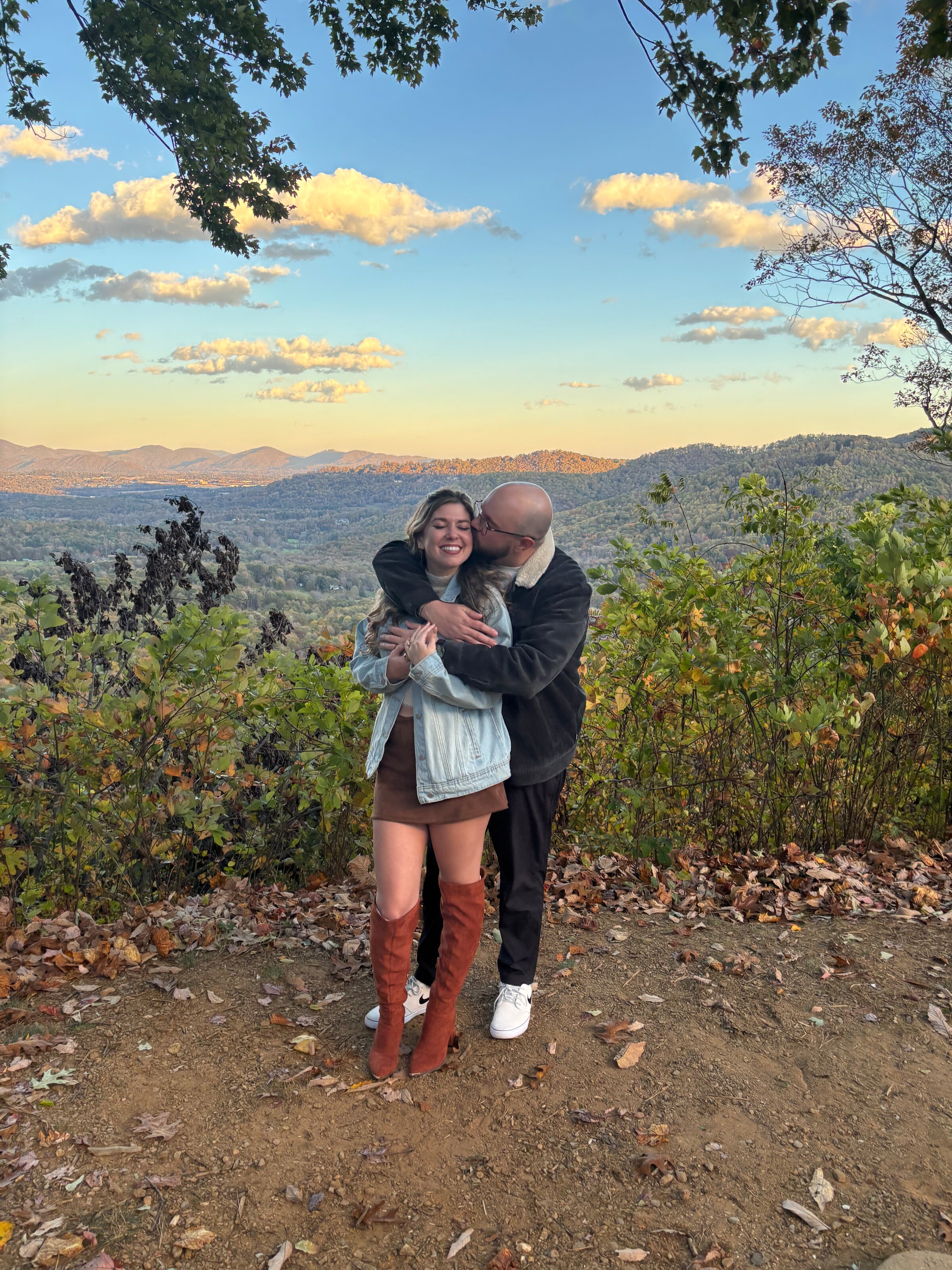 At the same overlook, one of them holding the other from behind, both laughing, autumn hills below.